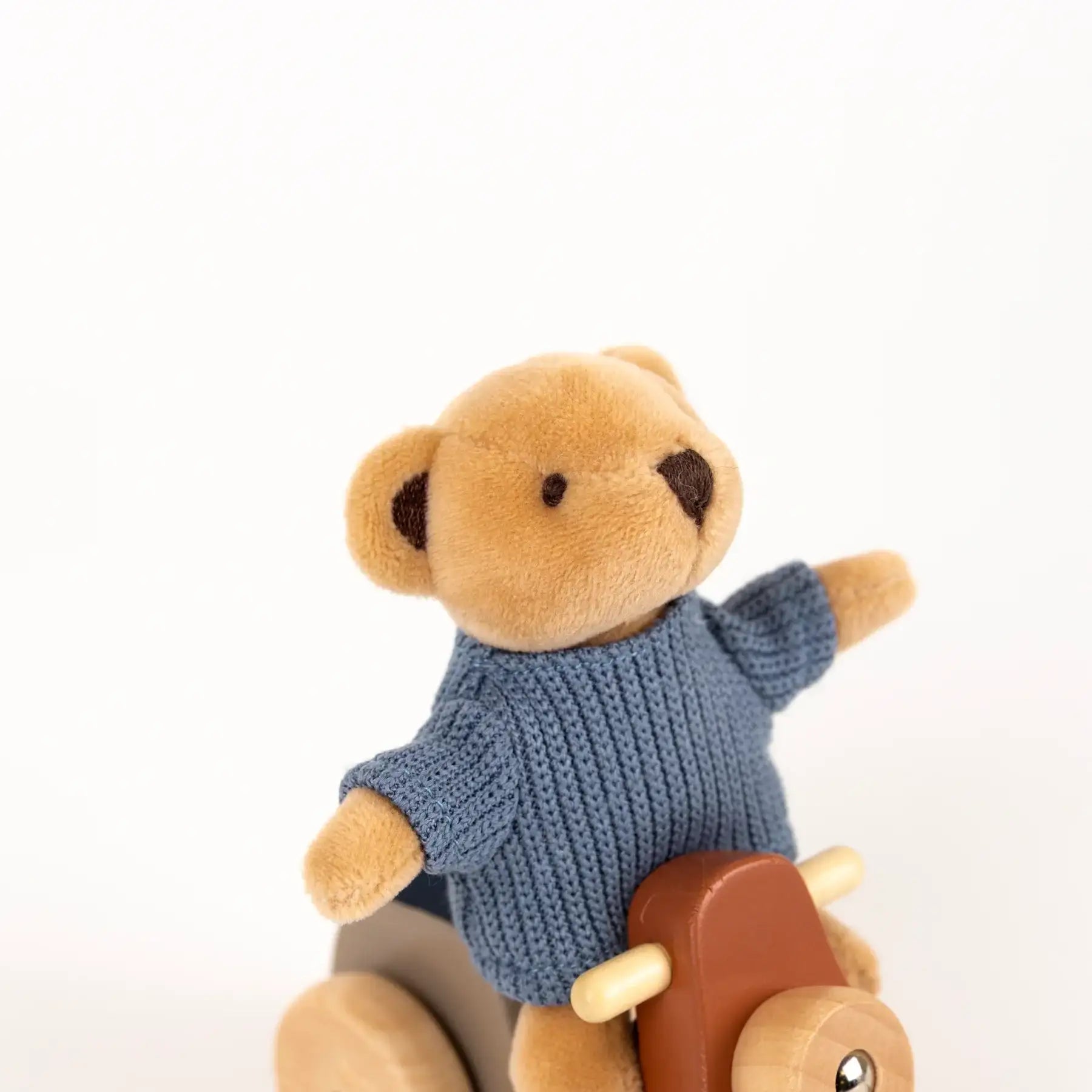Kuscheliger Teddybär in blauem Strickpullover auf Holzspielzeug, nachhaltiges Spielzeug für Kinder
