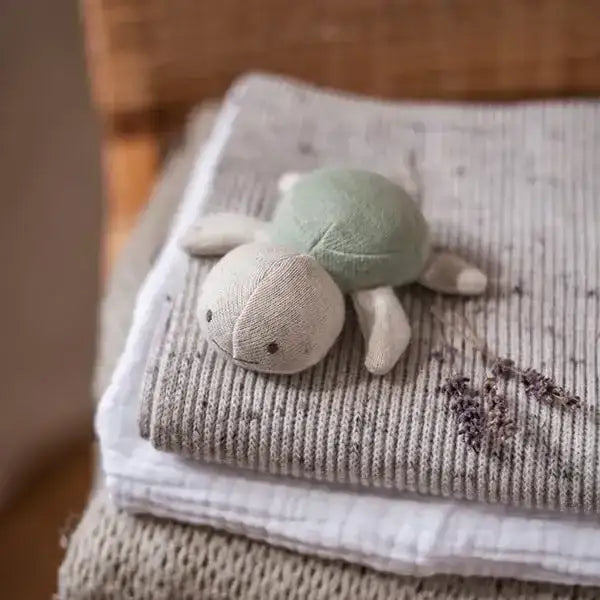 Grüne und beige Stoffschildkröte auf grauem gestricktem Tuch mit getrockneten Lavendelzweigen
