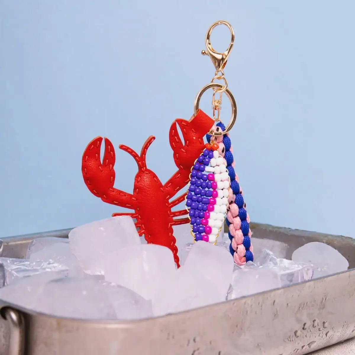 Roter Lederhummer Schlüsselanhänger mit Perlenfisch und geflochtenem Band, auf Eis im Metallbehälter
